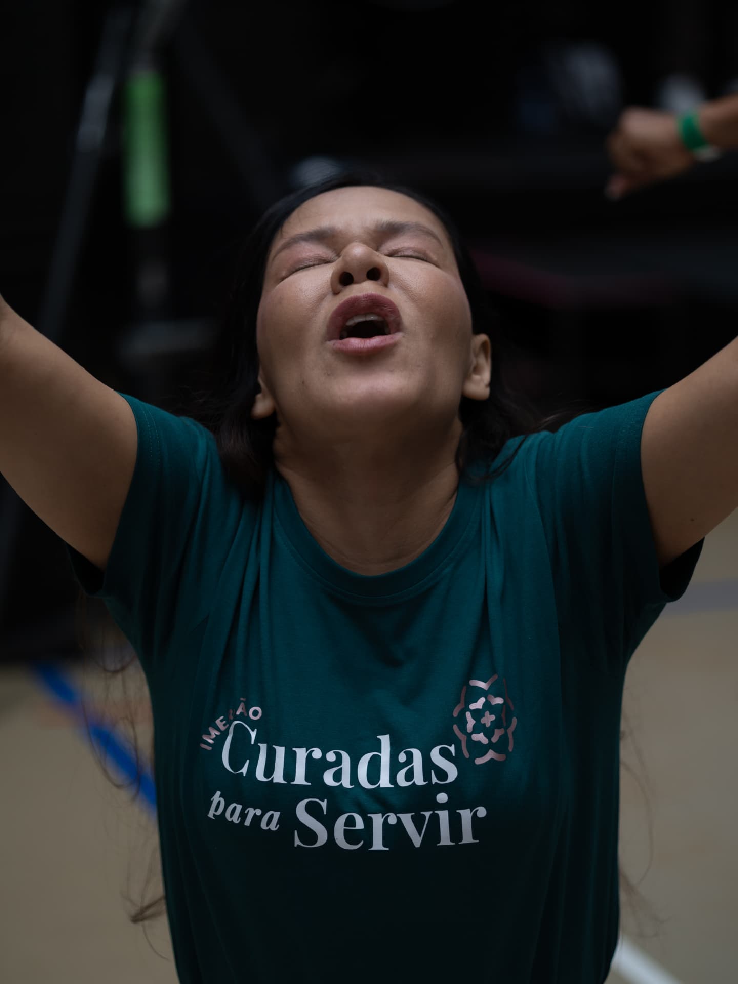 Mulher com camiseta Curadas para Servir e braços levantados em adoração